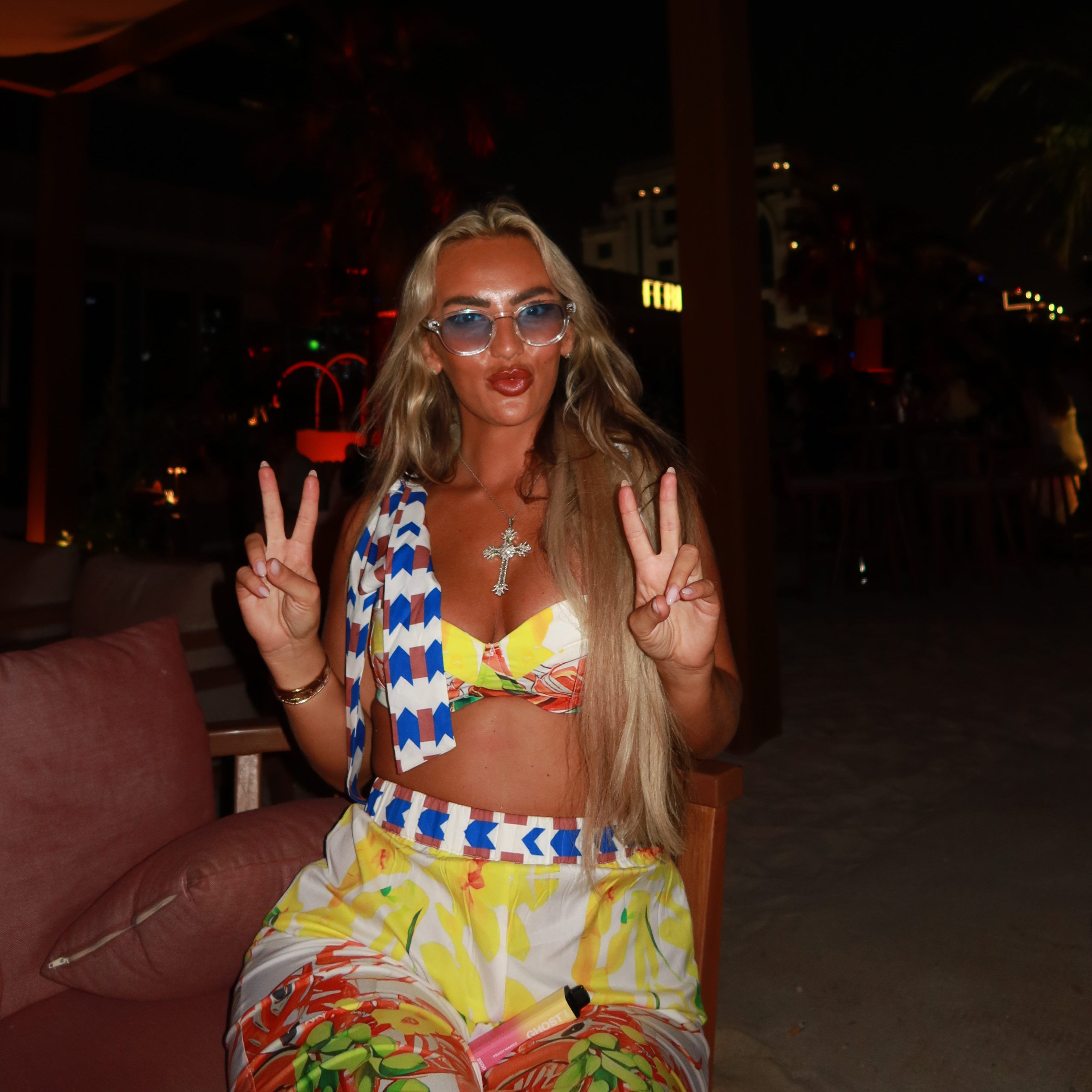 Fashion-forward woman wearing luxvizio Amsterdam sunglasses at a vibrant beach lounge by night – bold and colorful luxury eyewear with a touch of European street style and coastal glamour.